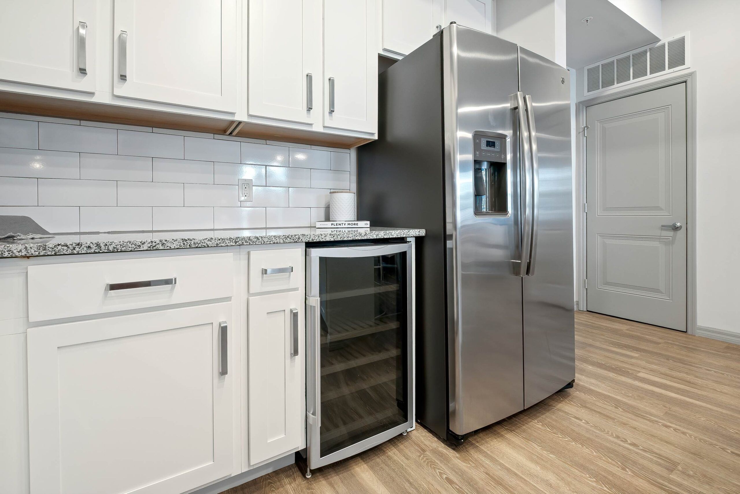 Inspira Naples Modern kitchen with white cabinets, stainless steel fridge, and a small glass-front wine cooler.