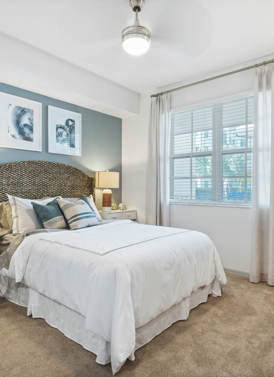 Inspira Naples Bright bedroom with a bed, desk, lamps, large window, and modern decor in neutral tones.