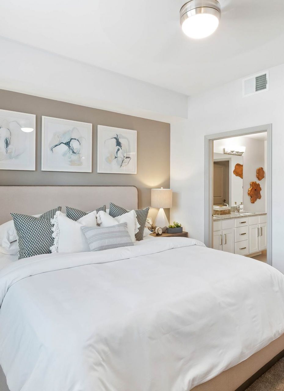 Inspira Naples Modern bedroom with a large bed, neutral decor, and an attached bathroom visible through an open door.