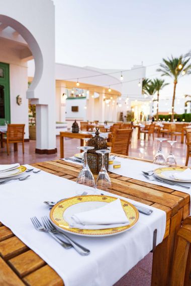 Inspira Naples Outdoor restaurant with wooden tables set for dining, surrounded by palm trees and string lights at dusk.