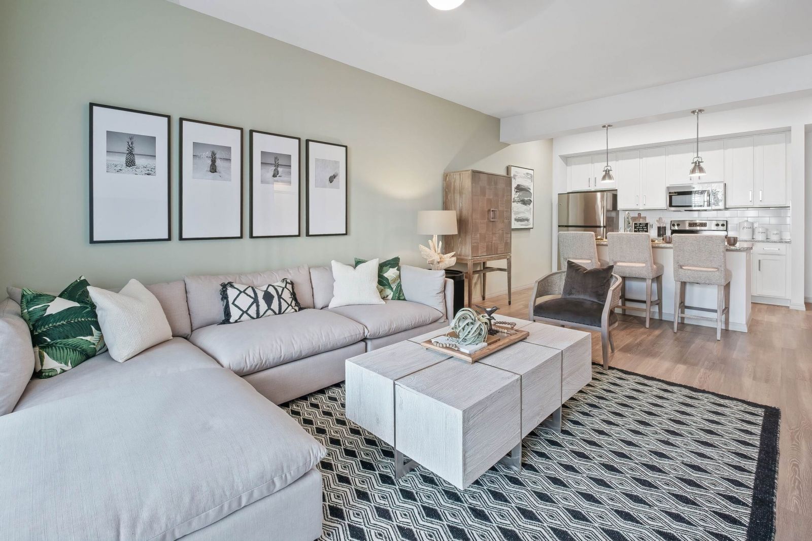 Inspira Naples Modern living room with light furniture, patterned rug, art on the wall, and an open kitchen in the background.