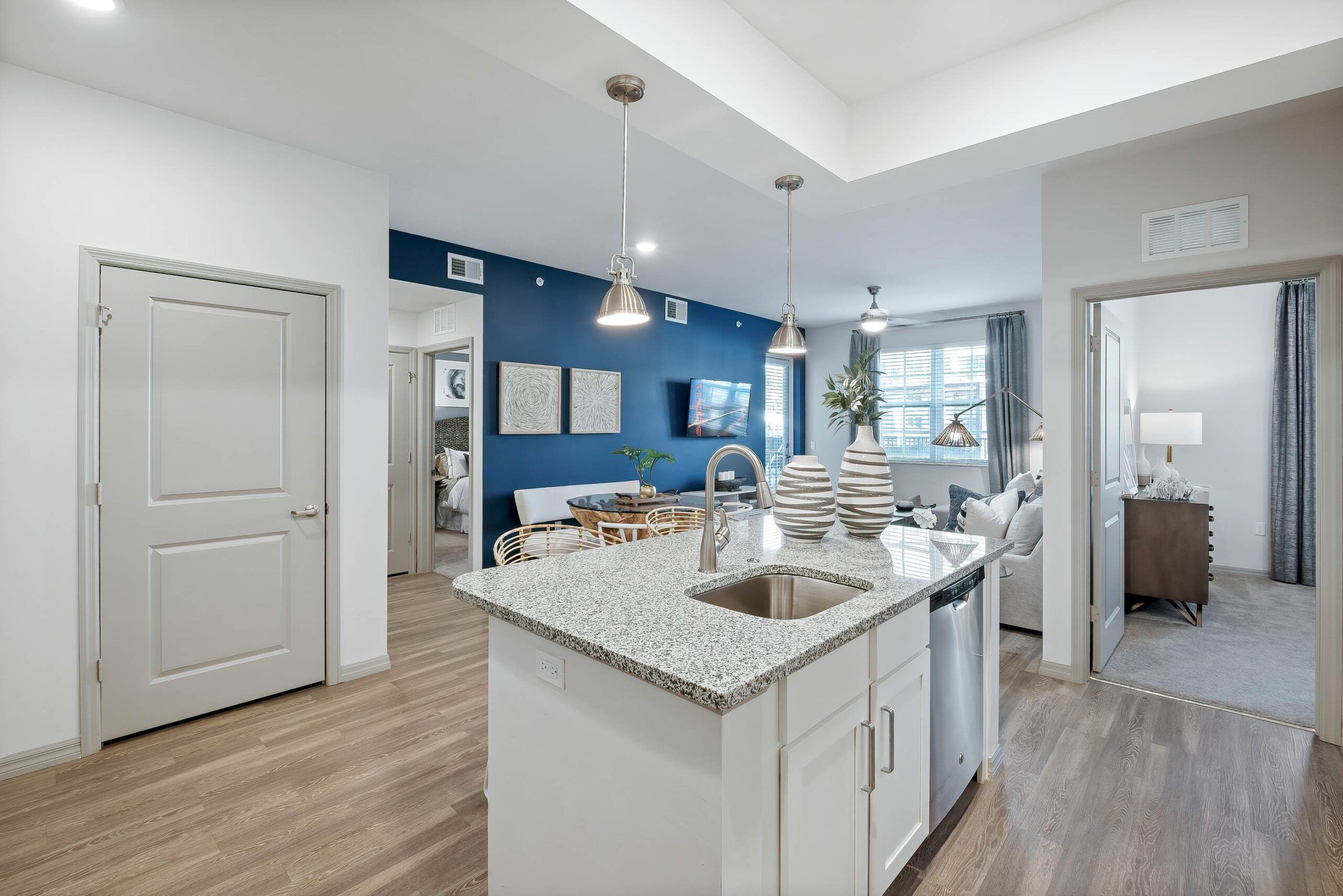 Inspira Naples Modern open-plan kitchen and living area with granite island, blue accent wall, and wood flooring.