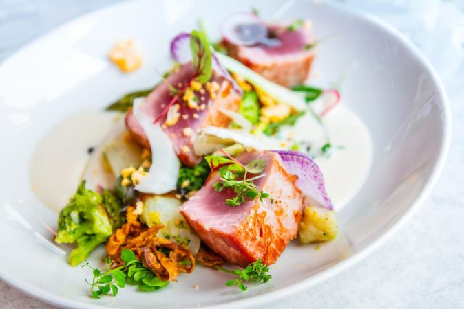 Inspira Naples Seared tuna on a white plate with vegetables, microgreens, and a creamy sauce, artfully arranged.